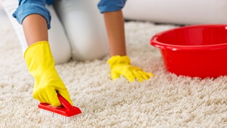 Mulher com luvas amarelas a lavar carpete com produtos de limpeza de carpetes e tapetes